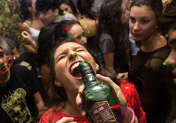 Exciting party scene with young adults enjoying drinks and dancing under colorful lights. HD wallpaper