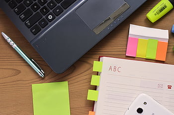 Top view of a workspace featuring a laptop, notebook, pen, and colorful stationery on a wooden desk. HD wallpaper