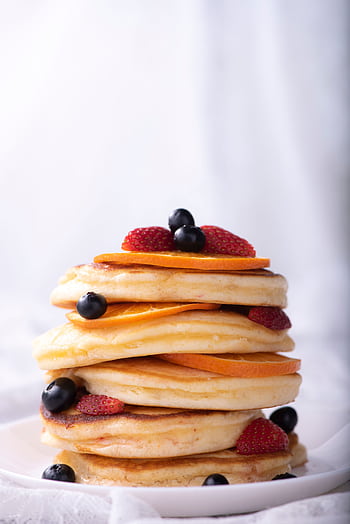 Tall stack of fluffy pancakes topped with blueberries, strawberries, and orange slices. HD phone wallpaper