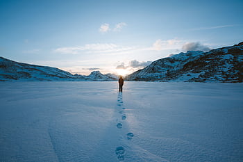 A person walking alone on a snowy landscape in Flakstad, Norway during winter. HD wallpaper