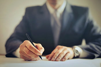 Faceless businessman in suit signing a contract at office desk, focused on task. HD wallpaper