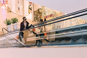 A fashionable woman ascends an escalator in a chic, modern shopping mall. HD wallpaper
