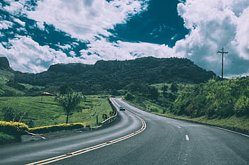 A que road winding through the countryside with mountains in the background under a blue sky. HD wallpaper