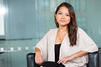 A professional Asian businesswoman sitting confidently in a modern office setting. HD wallpaper