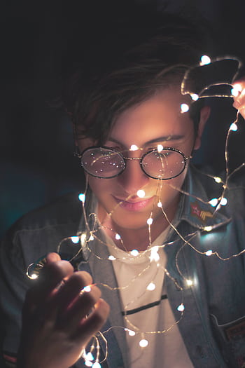 Young man with glasses illuminated by fairy lights, creating a stylish and artistic portrait. HD phone wallpaper