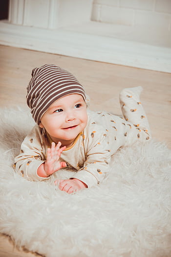 A cute baby in striped beanie lying on fluffy rug indoors, smiling with innocence. HD phone wallpaper