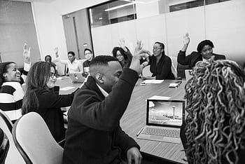 A diverse group of adults in an office meeting, engaged in a discussion with laptops, raising hands to vote onsomething. HD wallpaper