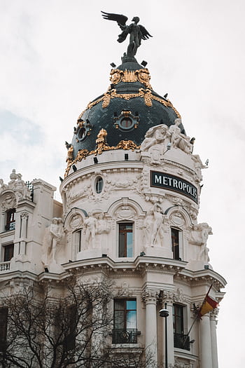 Iconic Metropolis Building dome in Madrid captured in daylight, showcasing intricate architectural details and sculptures. HD phone wallpaper