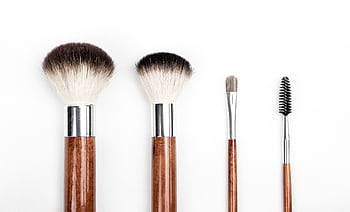 Stylish flat lay of four wooden makeup brushes against a clean white background. HD wallpaper