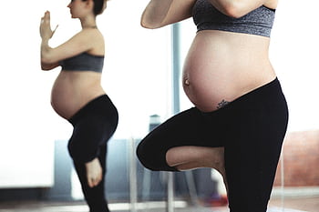 Pregnant woman doing yoga in front of mirror, promoting health and wellness. HD wallpaper