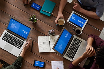 Top view of a diverse team using technology in a meeting. Laptops, tablets, and smarts on a wooden table. HD wallpaper