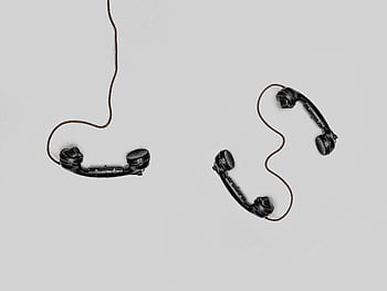 Two vintage black tele handsets connected by cords on gray background. HD wallpaper