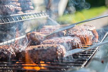 Close-up of sizzling beef burgers on a charcoal grill with flames and smoke. HD wallpaper