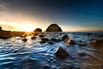 Peaceful sunrise over a rocky shoreline with calm ocean waters and a clear sky. HD wallpaper