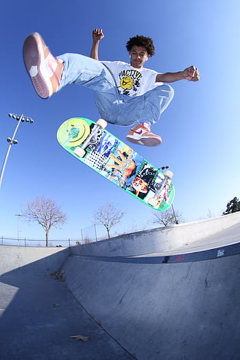 A dynamic of a teenager executing a mid-air skateboard trick in an urban skate park. HD phone wallpaper