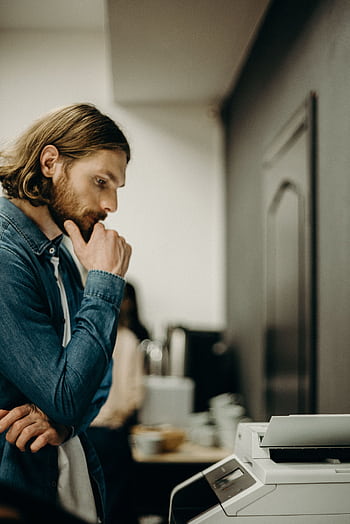 A man in deep thought while operating a printer in an office setting. HD phone wallpaper