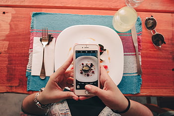 A woman takes a of a dessert with her smart at a restaurant. HD wallpaper
