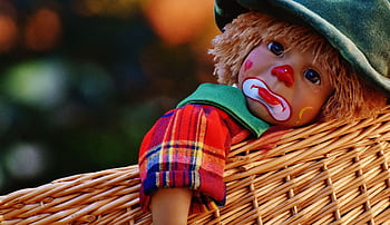 A close-up of a colorful clown doll with a sad expression lying in a woven basket. HD wallpaper