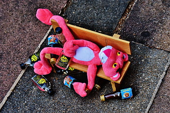 A pink plush toy sprawled on a bench with mini liquor bottles around it, creating a humorous scene. HD wallpaper