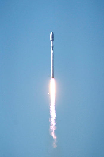 Falcon 9 rocket launching into space, showcasing powerful propulsion against a clear blue sky. HD phone wallpaper