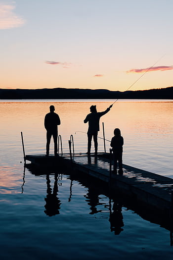 A serene scene of a family fishing together on a lake dock at sunset, creating silhouettes on the water. HD phone wallpaper