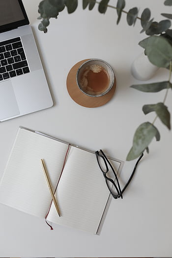 Minimalist workspace flat lay featuring a laptop, coffee cup, open notebook, and glasses. HD phone wallpaper