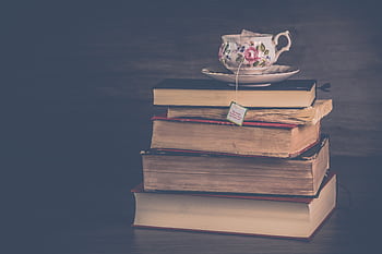 Elegant vintage teacup with floral design resting atop a pile of old books, evoking nostalgic charm. HD wallpaper