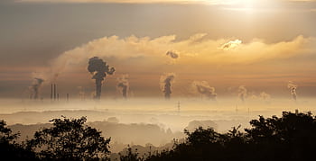 Smoke rising from factory chimneys at sunrise, symbolizing pollution and environmental impact. HD wallpaper