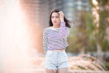 A teenage girl in a striped top and denim shorts enjoying a sunny day outdoors. HD wallpaper