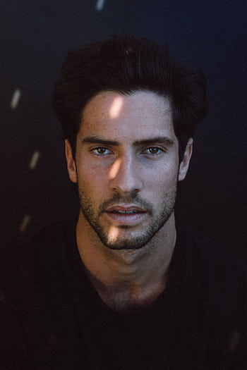 Intriguing close-up portrait of a young man with dark hair, featuring a thoughtful gaze. HD phone wallpaper
