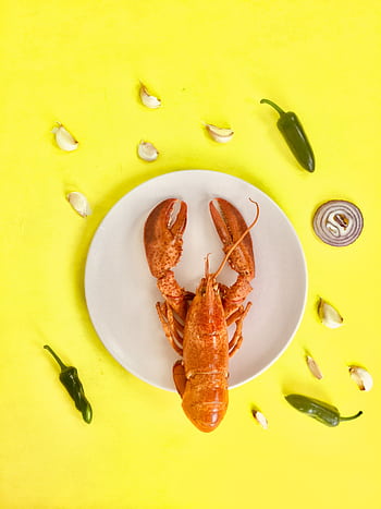 Top-down view of a lobster dish with garlic, peppers, and onion on a vibrant yellow background. HD phone wallpaper