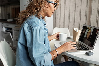 Woman enjoying a video call with a friend, sipping coffee at home. HD wallpaper