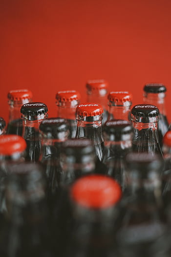 A close-up of Coca-Cola bottle tops with a focus on red caps against a red background. HD phone wallpaper