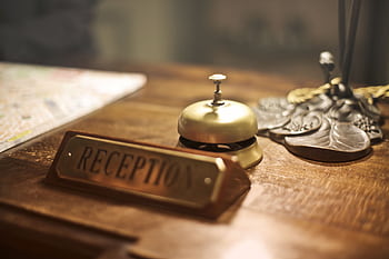 Classic hotel lobby reception desk with vintage bell and signage on wooden counter. HD wallpaper