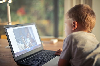 A young boy engrossed in watching content on a laptop in a cozy home setting. HD wallpaper