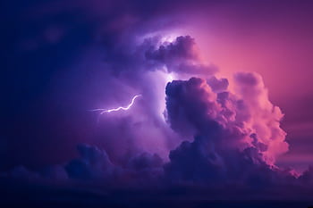A striking of lightning illuminating dramatic purple clouds in the night sky. HD wallpaper