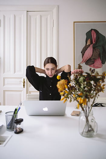 A woman focuses on work at a laptop in a minimalist home office setting with a flower vase. HD phone wallpaper