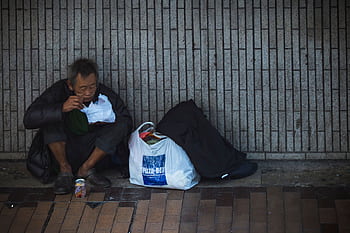 Elderly man sitting on city street, surrounded by bags, conveying solitude. HD wallpaper