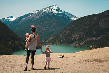A mother with two children enjoys a scenic mountain and lake view during a sunny outdoor hike. HD wallpaper