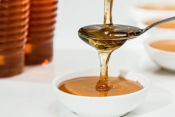 Delicious honey pouring slowly from a spoon into a white bowl, highlighting its golden hue and viscosity. HD wallpaper