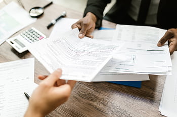 Two professionals exchanging documents in an office setting, focusing on paperwork and data analysis. HD wallpaper