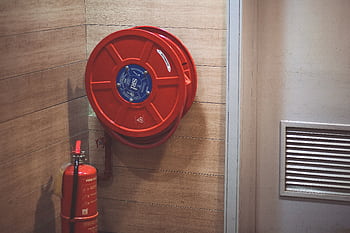 Red fire hose reel and extinguisher inside a building corner. HD wallpaper
