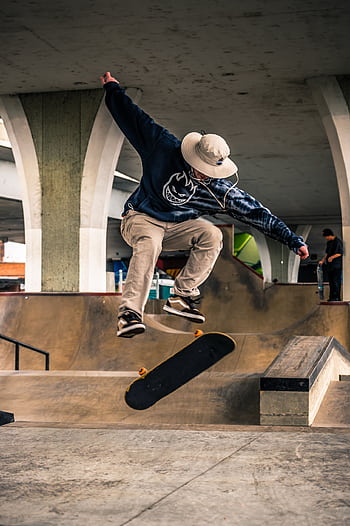 A skateboarder performs a high-energy trick in an urban skate park under a bridge. HD phone wallpaper