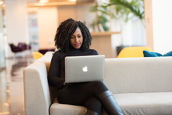 An African American woman working remotely on a laptop in a modern indoor setting. HD wallpaper