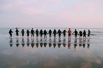 A large group holding hands at the beach during sunset, reflecting in the water. HD wallpaper