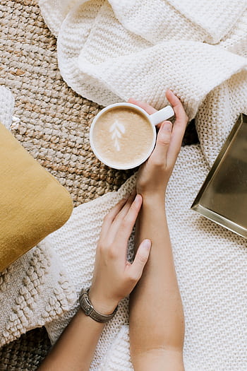 A serene morning scene featuring a hand holding a cappuccino with latte art on a cozy fabric. HD phone wallpaper