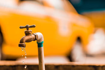 Macro shot of a brass faucet with water droplets against a blurred yellow background. HD wallpaper