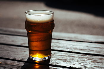 A cold pint of beer on a wooden table in a sunny outdoor setting, perfect for a summer day. HD wallpaper