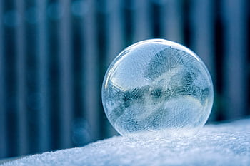 Close-up of a frozen bubble resting on a snow-covered surface during winter, capturing intricate frost patterns. HD wallpaper