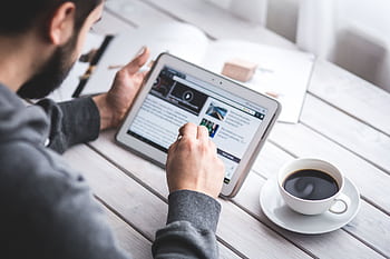 A man uses a tablet to browse news while enjoying a cup of coffee, stylus in hand. HD wallpaper